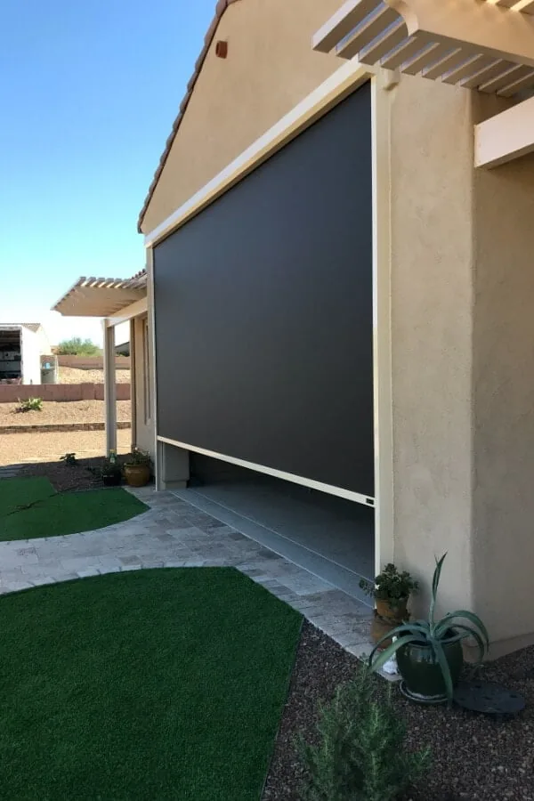 Charcoal on Turf, a charcoal solar shade lowered on a side patio under a white pergola beside artificial turf