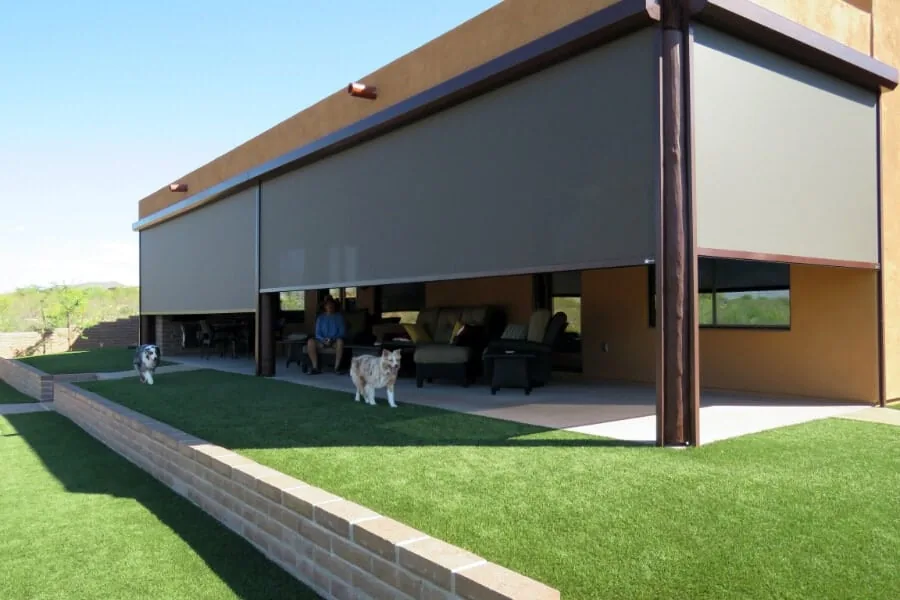 Full-Length Span, motorized solar shades lowered along the entire covered patio of a desert home with dogs on the lawn