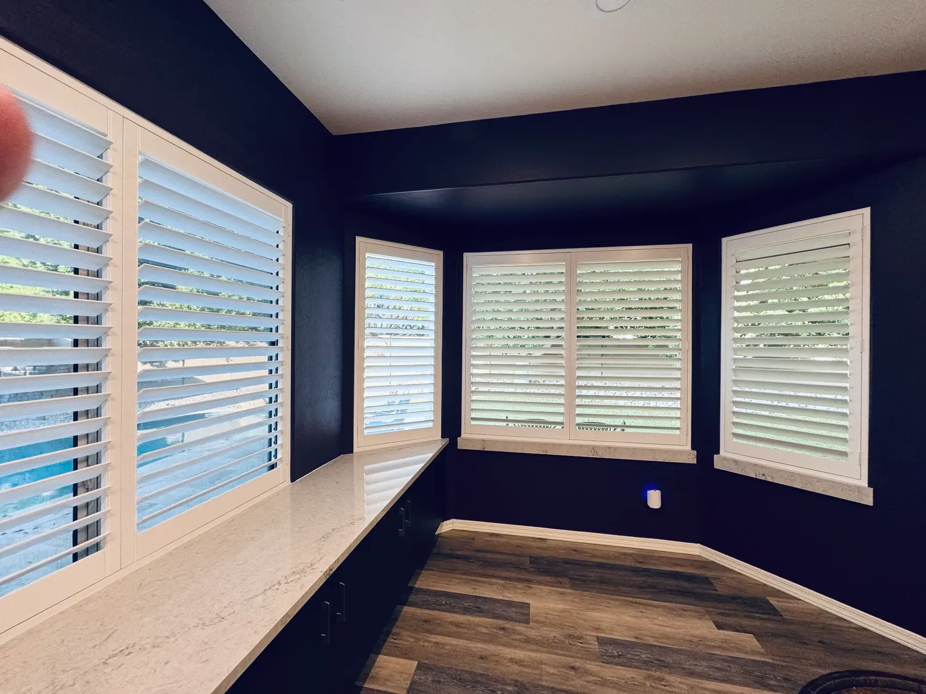 Home office bay window shutters, white louvers against navy walls and a quartz desk