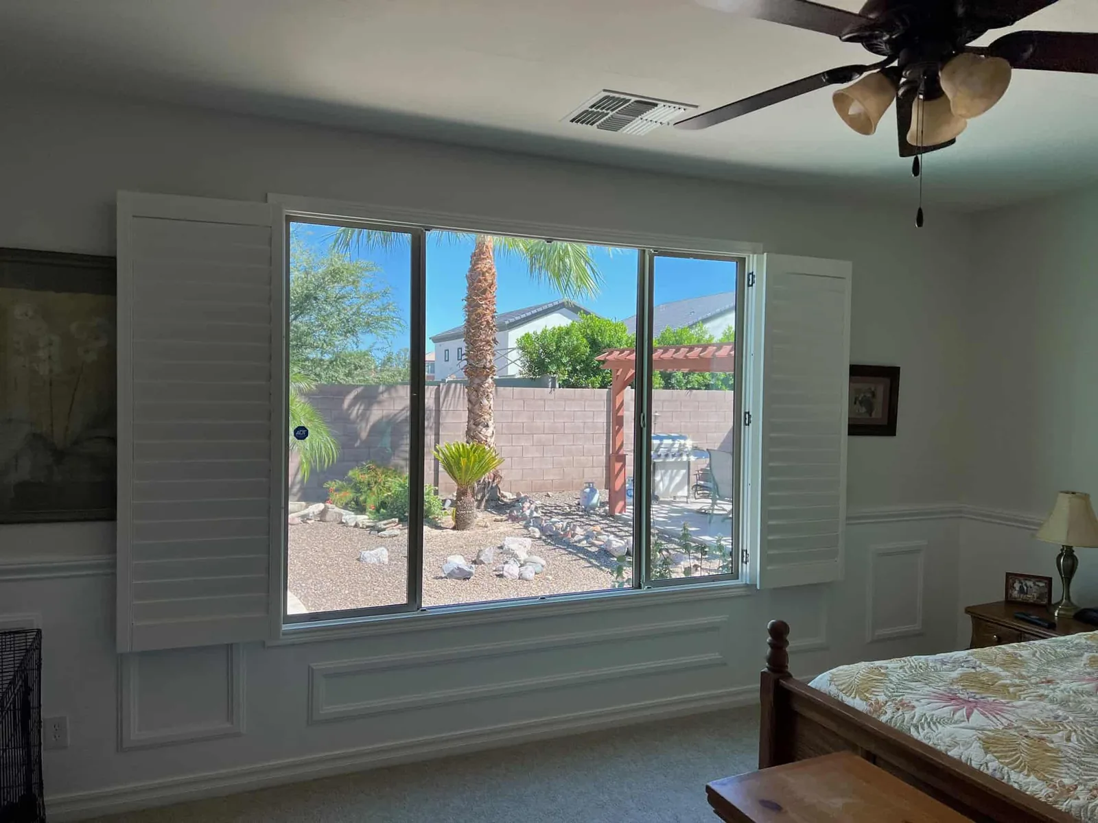 Plantation shutters on a wide window with a backyard view